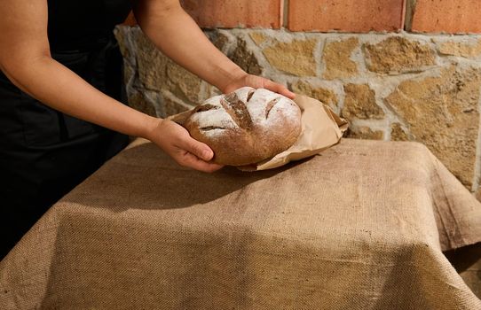 Close-up: Hands of a housewife or female baker, chef pastry holding warm homemade freshly baked whole grain wheat bread, rich in nutrient fibers and vitamins. Selective focus. Copy advertising space