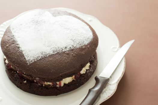 Freshly baked chocolate cake with a heart shape in icing sugar on the top symbolic of love and romance, anniversary or Valentines Day