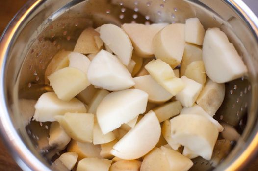 Diced fresh potatoes draining in a metal colander viewed top down close up in a food preparation concept