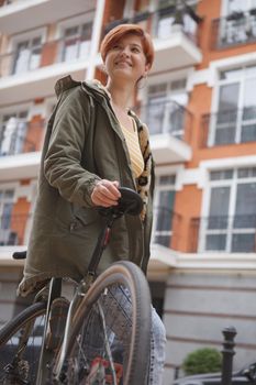 Low angle vertical shot of a cheerful young woman leaning on her bicycle