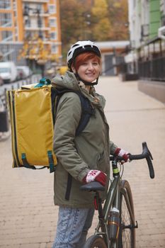 Vertical shot of a cheerful young woman working on her bicycle as delivery service courier