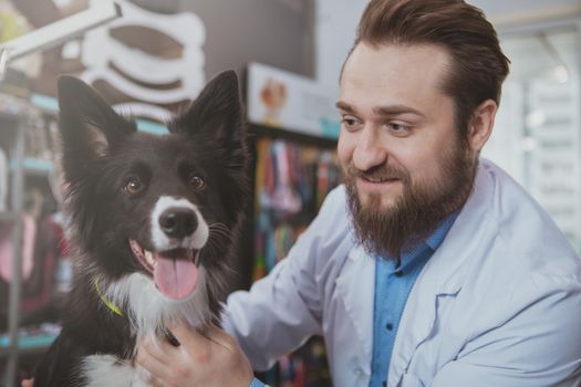 Close up of a cheerful vet doctor smiling at cute happy healthy dog after medical checkup. Adorable puppy being examined by professional veterinarian