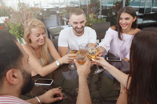 Group of friends clinking glasses, drinking at rooftop restaurant