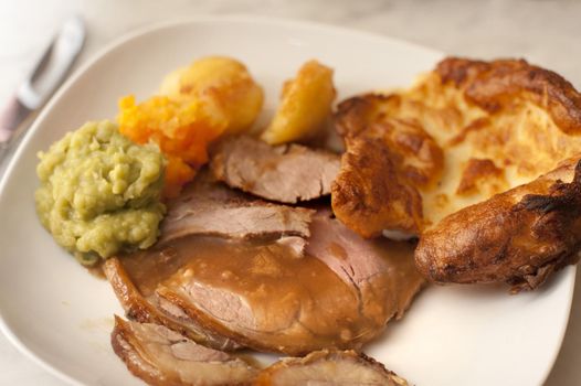 Delicious sliced roast beef and Yorkshire pudding served with gravy and vegetables for a tasty dinner, close up of the plate of food