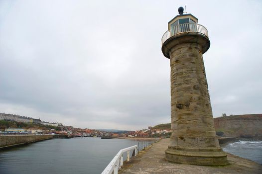 Old stone lighthouse on the end of the pier in Whitby harbour to act as a navigation guide and warning for shipping