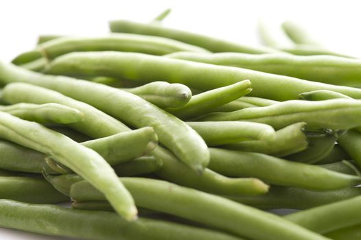 Heap of whole fresh green uncooked string or runner beans viewed low angle over white