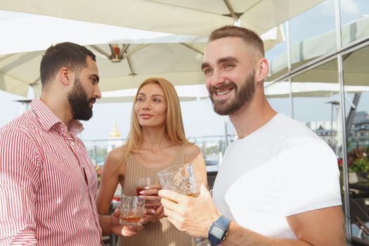 Attractive young man smiling, looking away joyfully enjoying summer rooftop party at the bar