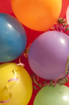 Close up Colored Birthday Party Balloons with Streamers Against Red Background