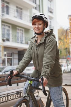 Vertical shot of a happy young woman wearing bike helmet, riding bicycle in the city