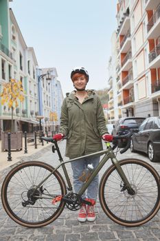 Vertical full length shot of a lovely young stylish woman posing with her bicycle, wearing protective helmet