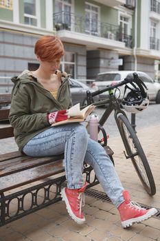 Vertical full length shot of a woman studying outdoors in the city, resting after cycling