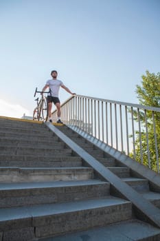 Vertical shot of a male athletic cyclist standing with his bike on top of the stairs in the city, copy space