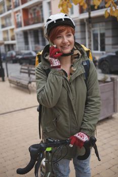 Vertical shot of a happy young woman talking on her smart phone working as delivery courier on her bicycle