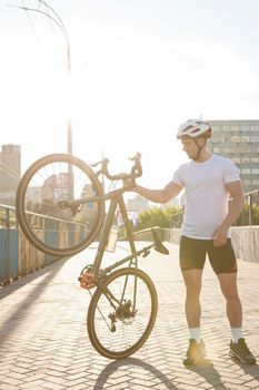 Vertical full length shot of a male cyclist lifting his bike, standing on city street