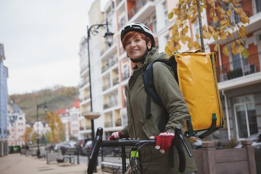 Charming female courier wearing biking helmet while working in the city on her bicycle