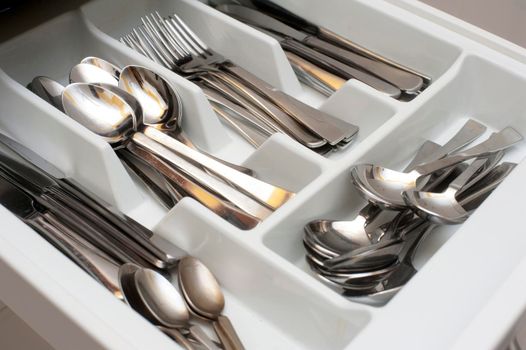 Open cutlery drawer in a kitchen unit with separate divisions for spoons, forks and knives