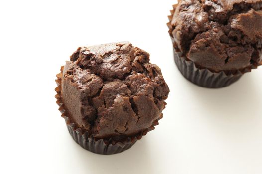 Two freshly baked dark chocolate muffins or cupcakes on a white background with copy space, high angle view
