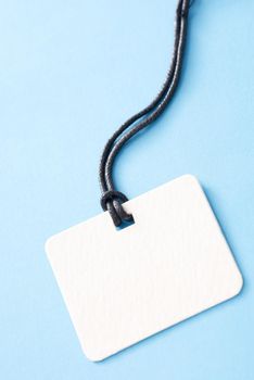 Close up of an empty white name tag table and string lanyard isolated on a plain blue background with copy space.