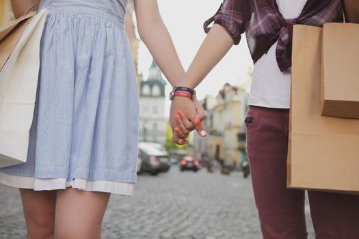 Cropped shot of two women holding hand, walking in the city with shopping bags. Female friends enjoying sightseeing on their vacation, holding hands