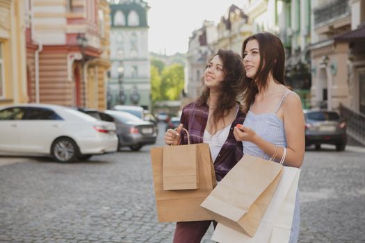 Two young happy women sightseeing together after shopping on their vacation, copy space. Beautiful woman and her friend walking in the city with shopping bags
