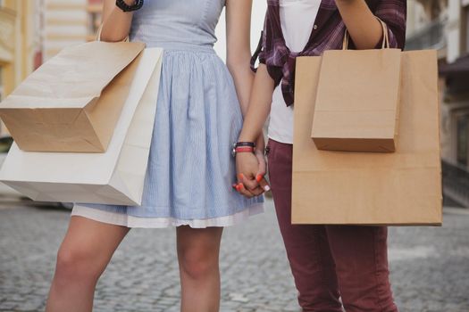 Cropped shot of two women carrying shopping bags, holding hands while walking. Two female friends walking in the city holding hands