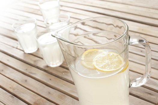 Fresh homemade lemonade in a jug with full glasses on an outdoor wooden picnic table for a refreshing summer beverage, high angle view