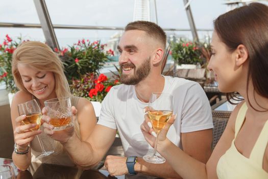 Group of friends laughing, drinking wine together at rooftop bar