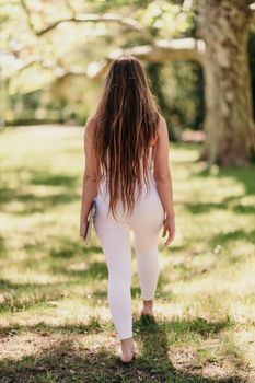 back view of a beautiful woman in a white tracksuit walking in the park with a laptop.