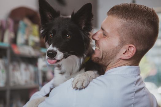 Close up of a happy cute dog hugging with vet doctor. Rear view shot of a handsome cheerful male veterinarian holding adorable healthy dog. Medicine, healthy pets concept