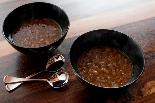 Two bowls of delicious homemade brown French onion soup served as a starter to dinner on a wooden table