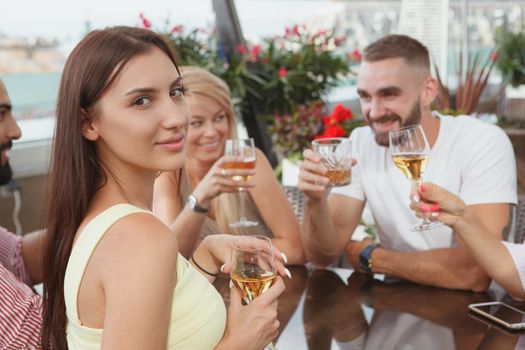 Attractive woman smiling to the camera while drinking with her friends at at rooftop bar