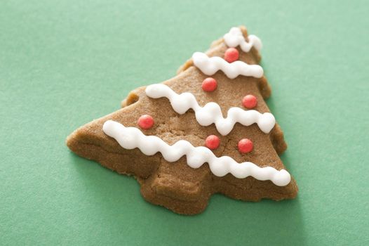 Christmas tree gingerbread cookie decorated with red and white icing on a green background with copy space