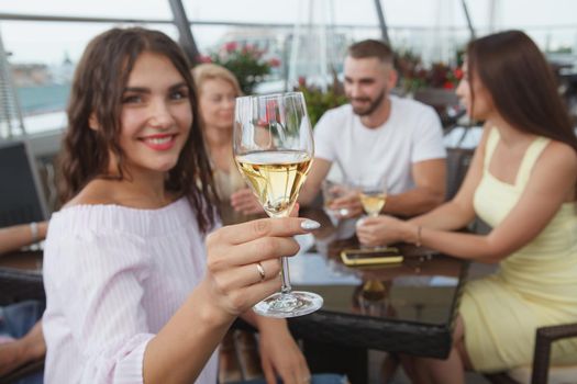 Selective focus on a wine glass in the hand of cheerful woman drinking with friends