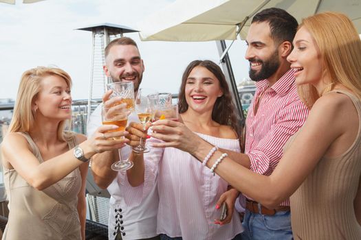 Happy young people screaming joyfully, toasting with their glasses, celebrating on a rooftop party