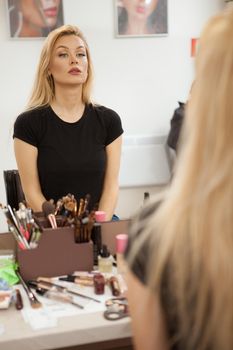 Vertical shot of a beautiful woman sitting in front of the mirror at makeup studio