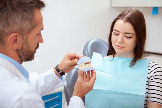Charming young woman visiting dentist. Mature male dentist showing his patient teeth mold