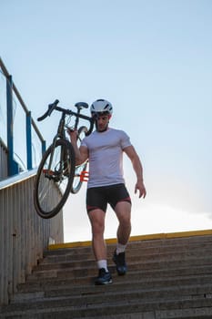 Vertical low angle shot of a muscular cyclist carrying his bike down the stairs outdoors