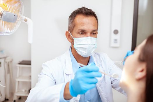 Professional dentist wearing medical mask, examining teeth of a patient