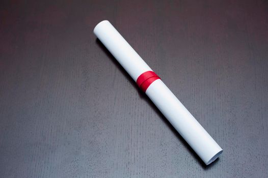 Educational background of a rolled graduation certificate tied with a red ribbon lying on a grey background with copysapce
