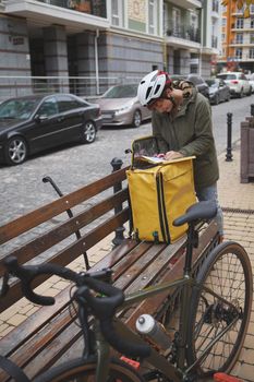 Vertical shot of a female courier filling papers outdoors, wearing biking helmet