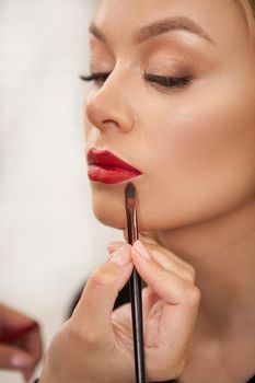 Vertical shot of a makeup artist applying red lipstick on the lips of a female client