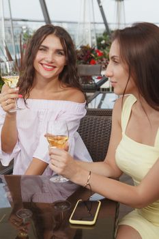 Vertical shot of two beautiful women drinking together at rooftop bar