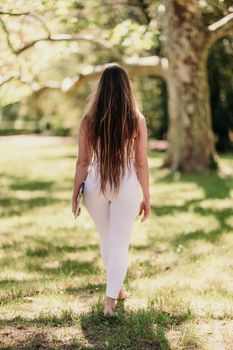 back view of a beautiful woman in a white tracksuit walking in the park with a laptop.