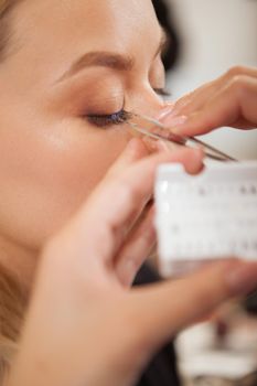 Vertical close up of a woman getting false eyelashes applied by professional makeup artist