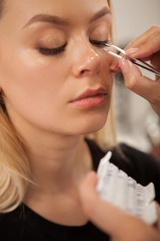 Vertical close up of a beautiful woman getting false lashes glued by professional makeup artist