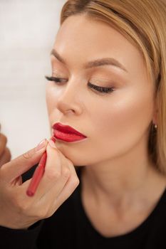 Vertical portrait of a gorgeous woman having her lips painted red by makeup artist