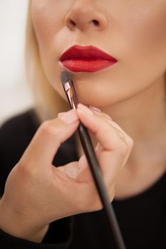 Vertical cropped shot of a makeup artist using concealer around the lips of a woman with red lipstick