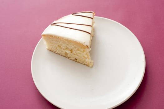 Single slice of freshly baked tasty cake with decorative icing on a plate over a deep pink background , high angle view