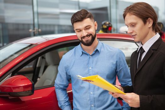 Cheerful bearded man talking to car dealer, buying new automobile at the dealership, copy space