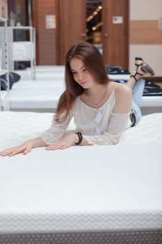 Vertical shot of a lovely woman lying on new orthopedic bed at home goods store